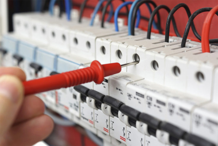 Hand of electrician with multimeter probe at electrical switchgear cabinet